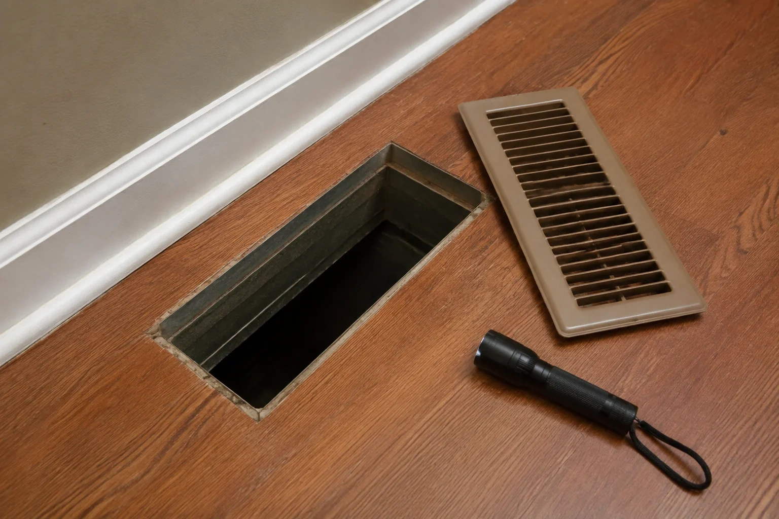 Removed floor register beside an open metal register boot and a flashlight.