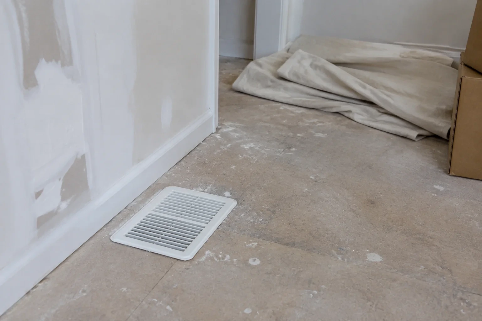 White floor register beside a patched wall and renovation dust on the floor.