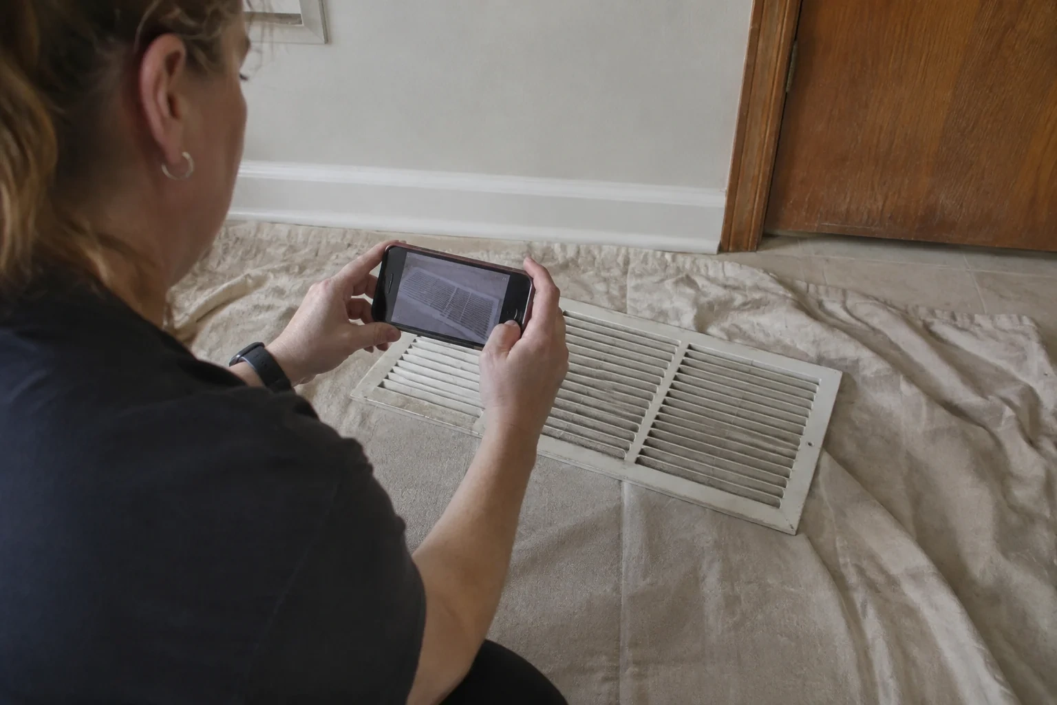 Technician photographing a removed return grille resting on a protective cloth.